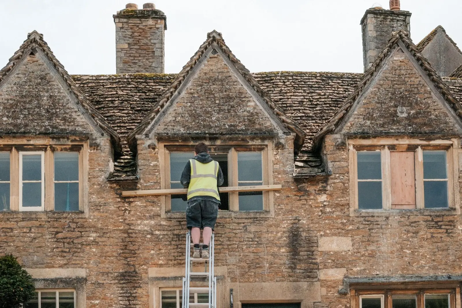 Maçon sur une échelle, réparant la façade en pierre d'une maison ancienne