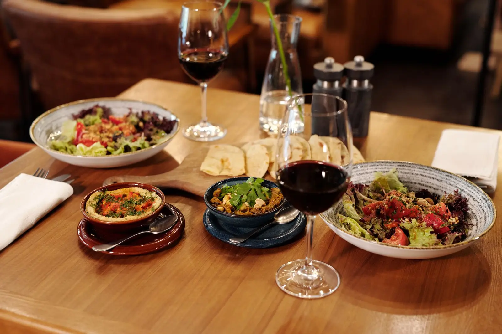 Table dressée en bois, deux assiettes de salade et des verres de vin rouge
